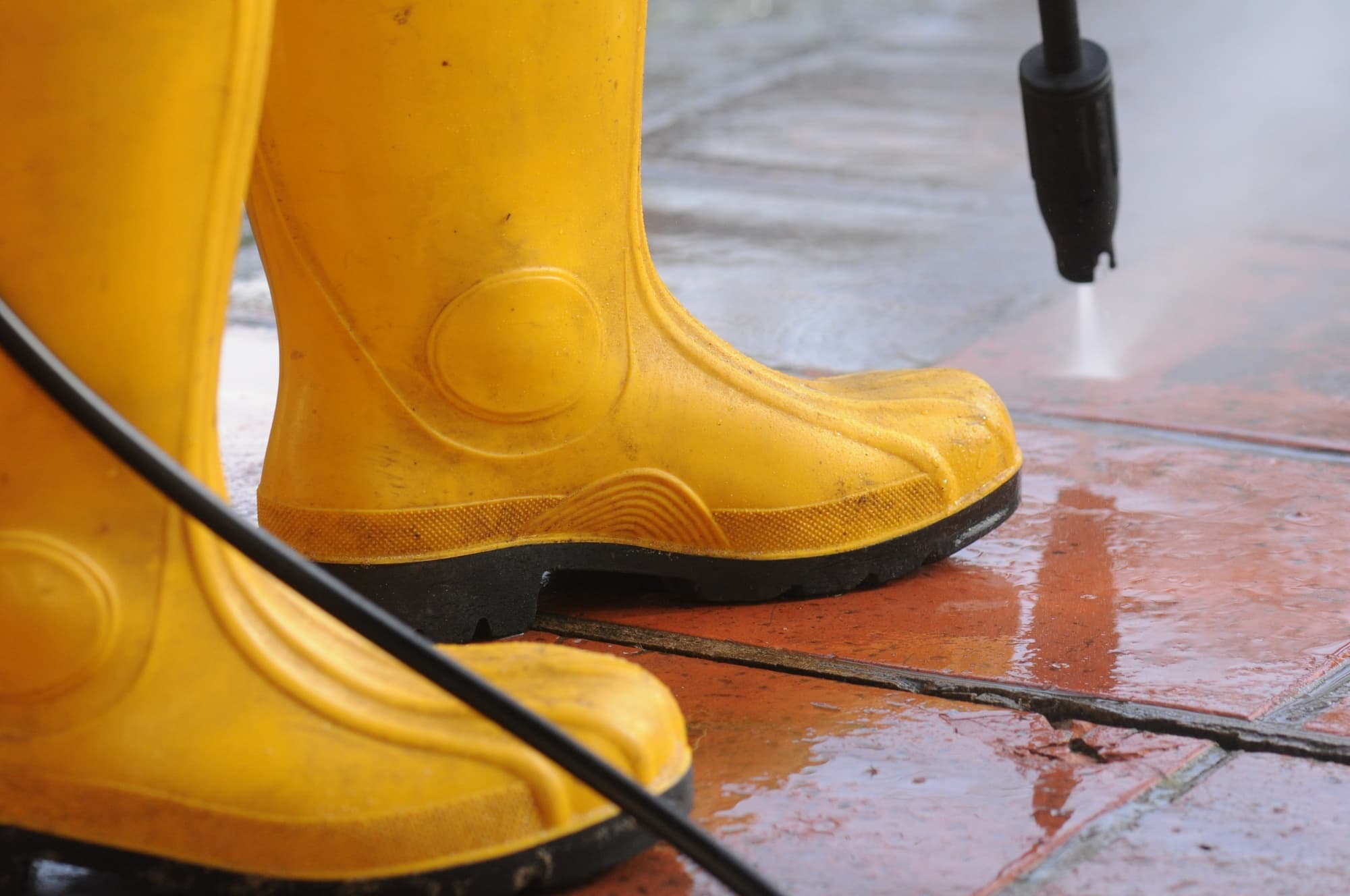 Yellow boots beside a pressure washer cleaning wet terracotta tiles